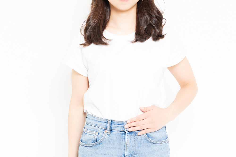 白いTシャツ姿でお腹に手を当てる女性