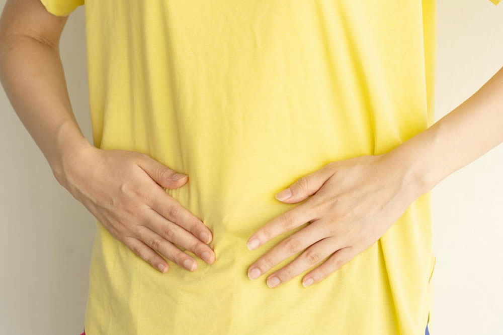 黄色い服の上からお腹に両手を当てる女性
