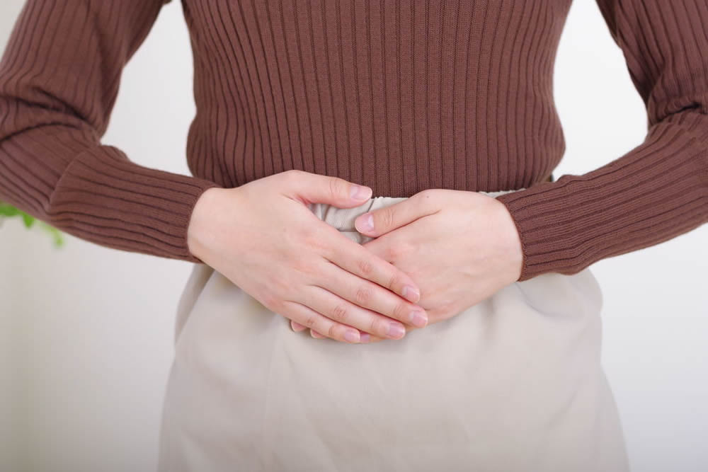茶色の長袖ニット姿でお腹に両手を重ねる女性