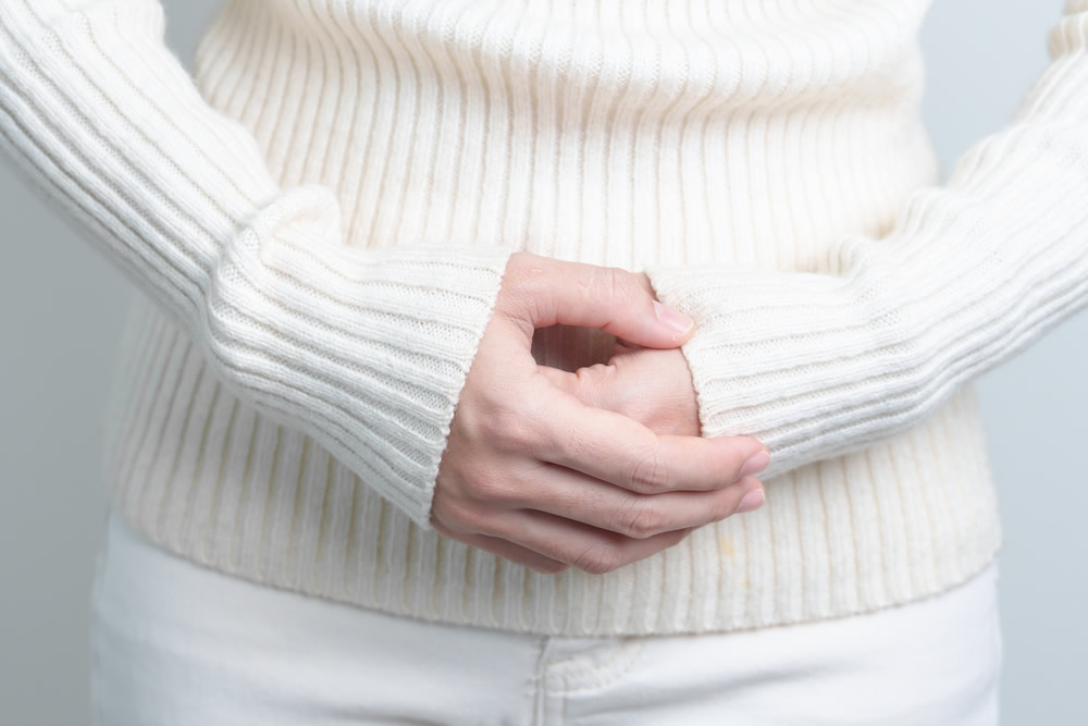 白いニット姿でお腹に手を当てる女性