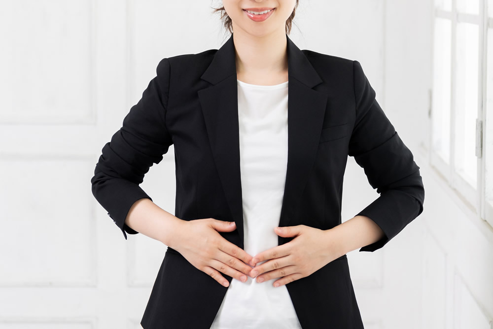スーツ姿でお腹に手を当てる女性