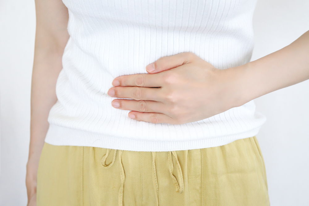 白いトップスと黄色いボトムを着てお腹に手を当てる女性