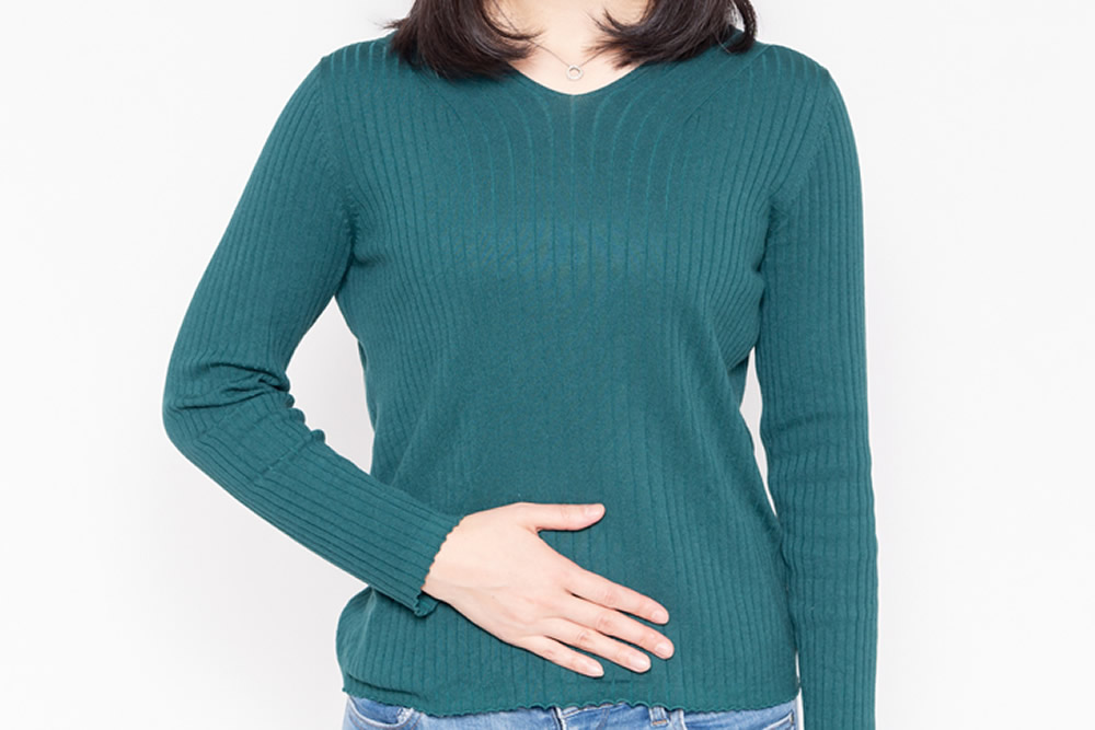 緑色の服でお腹に手を当てる女性