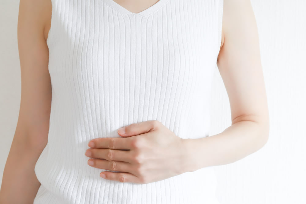 白いノースリーブ姿でお腹を片手で押さえる女性