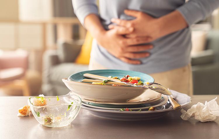食べすぎた後に胃の調子が悪くなった人と食事後のお皿の画像