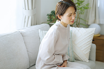 便秘でお腹を抑え、辛そうにする女性