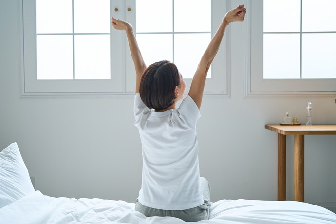 窓際でベッドの上で手を上げている女性