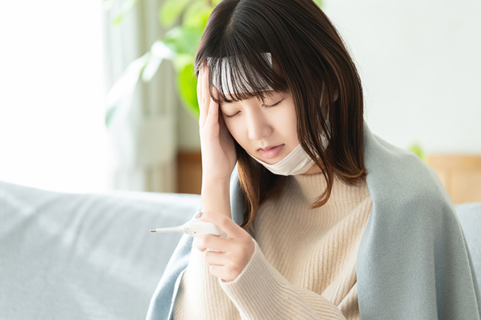 熱が出てソファで頭を押さえている女性