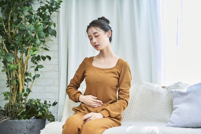 椅子に座って胃に不快感があって胃をおさえている女性